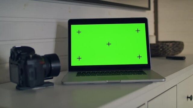 View of a table with a laptop computer with a green screen.