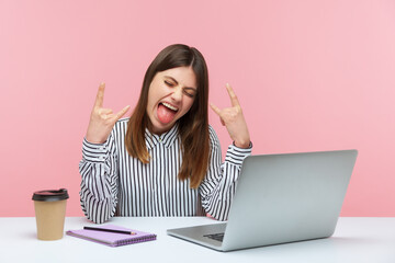 Positive naughty woman blogger showing rock and roll finger gesture looking at laptop display,...