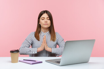 Open minded brunette woman office worker in striped shirt pressing hands together meditating at workplace, preparing herself for work. Indoor studio shot isolated on pink background