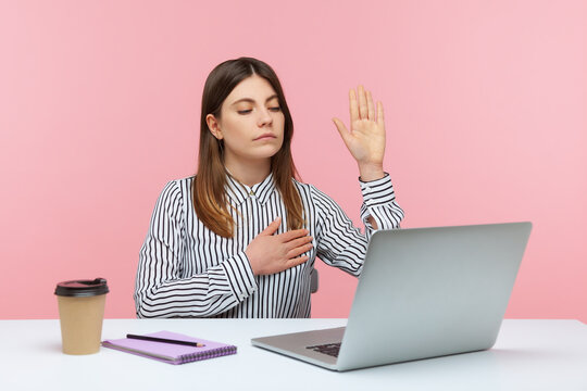 I swear! Responsible woman office worker giving promise holding hand on heart, looking at laptop screen, talking on video call, online conference. Indoor studio shot isolated on pink background