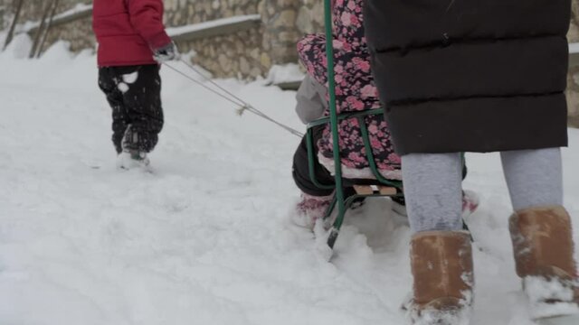 vacation, game, family concept - slo-mo authentic three happy preschool toddler kids siblings with young wonan mom sledding and play with snow. snowfall in cold season weather in winter yard outdoors