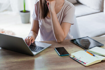 Young woman using laptop to work home, multiple devices