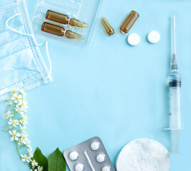 White tablets, glass ampoules, a syringe and cherry blossoms are arranged on alight blue...
