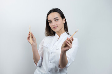 A young brunette girl holds an ecological toothbrush in her hands. A girl in a white coat promotes zero waste.
