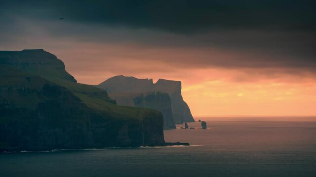 Time lapse of sunset at the north coast of Eysturoy with cliff layers and rock formation Risin og Kellingin and dark clouds over the ocean, Kalsoy Faroe Islands
