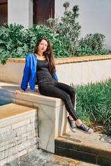 Portrait of a young brunette girl sitting near a fountain in the park