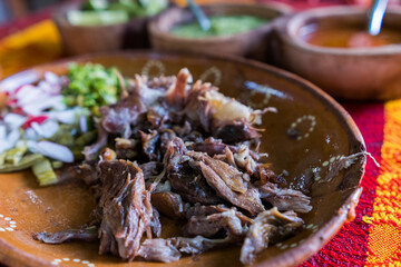 Mexican chopped lamb meat, hot sauces, and lime slices in clay bowls