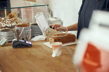 Female barista at showcase with desserts in cafe. Young worker of sweet shop and cafe