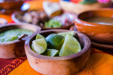 Bowls of lime slices, green sauce, and lamb broth on colorful tablecloth