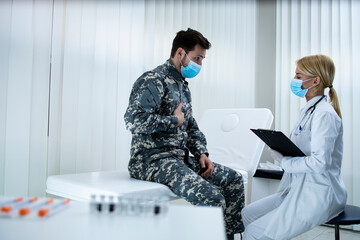 Soldier in uniform with face mask complaining on chest pains to the doctor. Military healthcare.