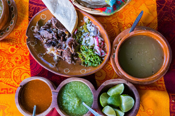 Obraz na płótnie Canvas Mexican chopped lamb meat, hot sauces, and broth on colorful tablecloth