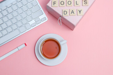 Cup of tea with a gift for fool's day and a keyboard on a pink background, top view close-up.