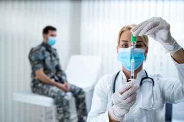 Vaccination of the military against corona virus. Doctor holding bottle and syringe and preparing vaccine shot for the soldier in uniform during corona virus epidemic.