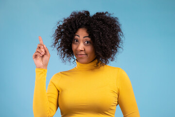 Portrait of african thinking pondering woman having idea moment pointing finger up on blue studio background. Smiling happy girl showing eureka gesture.