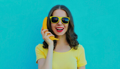 Portrait of funny woman calling on a banana phone on a blue background