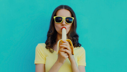 Portrait of young woman eating banana on a blue background