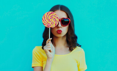 Portrait of young woman blowing her red lips with lollipop on a blue background