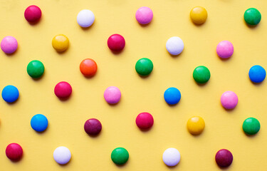 Colored balls of sugar on a yellow background. Chocolate candies covered with multicolored sugar glaze.