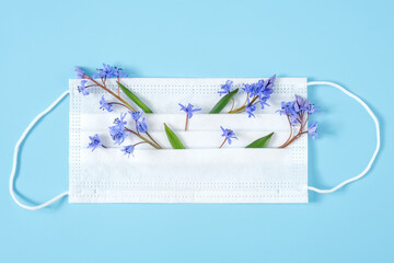 Medical face protective mask with springtime snowdrop flowers on blue background. Allergy concept, top view, flat lay, copy space, minimal composition