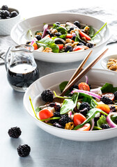 Close up of blackberry spinach salads with balsamic vinaigrette, against a bright sunny window.