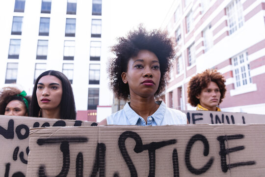 Three diverse male and female protesters on march holding homemade protest signs looking away