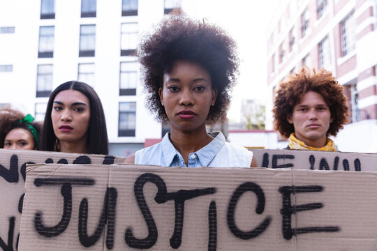 Three diverse male and female protesters on march holding homemade protest signs looking to camera