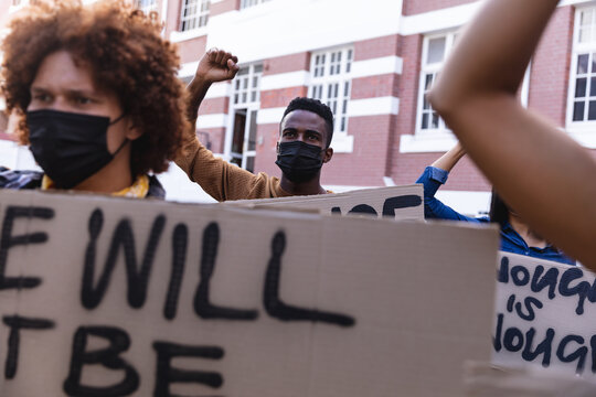 Diverse male and female protesters on march in face masks holding protest signs and raising fists