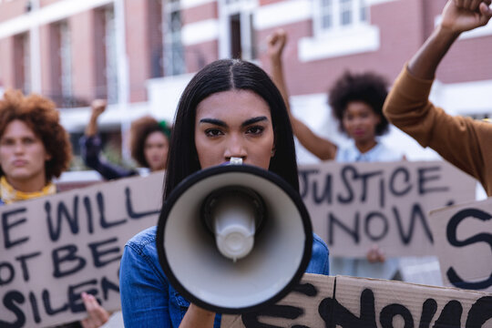 Mixed race woman using megaphone with protesters on march holding protest signs and raising fists