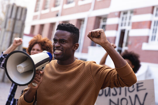 African american man using megaphone with protesters on march holding signs and raising fists