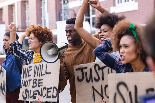 Diverse male and female protesters on march holding protest signs, shouting and using megaphone