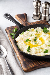 Close up of mashed potatoes in a cast iron skillet on a wooden board with salt and pepper shakers in behind.