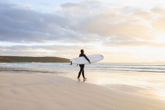 young woman heading into the surf carrying long board