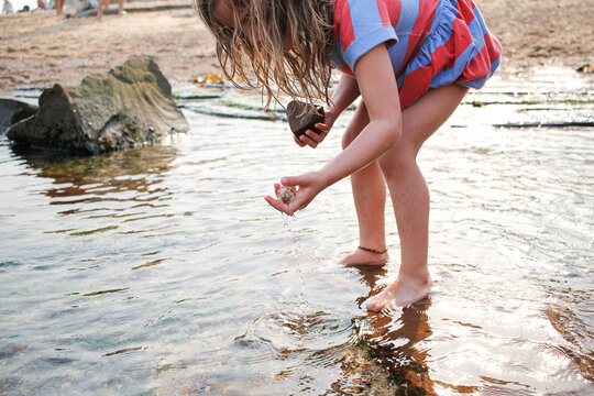 Young girl looking for shells and rocks in the shallow waters at the beach