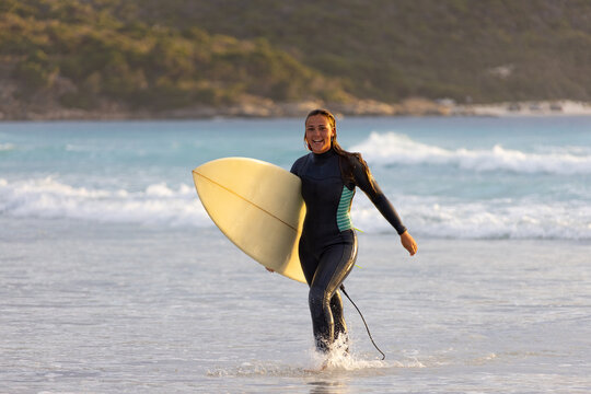 Person walking out of the water carrying surfboard on beach