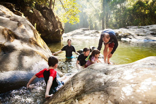 Happy Aussie family with young kids playing in cool water of creek in summer