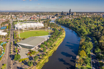 Aerial view of a wide river winding through a city with parkland and sporting facilities along side