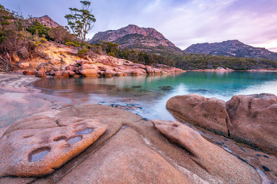 Sculptured granite rocks around a still bay with large mountains behind at twilight