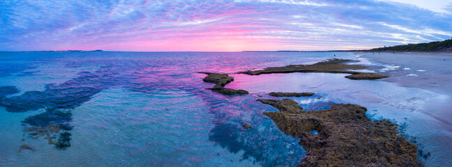 Aerial panoramic view of a vid purple sunset over calm rock pools