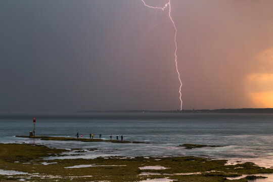 Lightning strikes as rain falls during thunderstorms over fishermen on a rocky outcrop