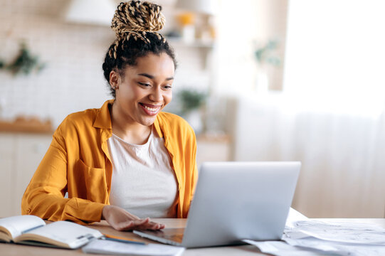 Smart attractive happy mixed race black girl with dreadlocks, in casual clothes, studying remotely, watching online briefing, talking on conference call with teacher or colleagues, smiling