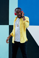 black guy in yellow shirt and red headphones laughing standing next to a colorful wall