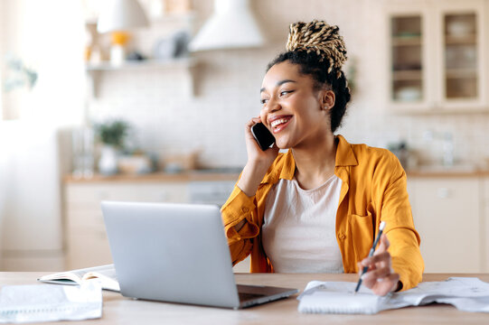 Happy successful busy young african american woman, broker, manager or freelancer working remotely, have pleasantly conversation with client or employee on the phone looking away smiling friendly