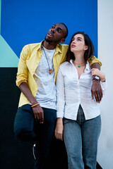 couple of young multiethnic men standing and hugging next to a very colorful wall, black boy and white girl in love,