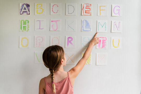 Rear view of girl (8-9) looking at alphabet on wall