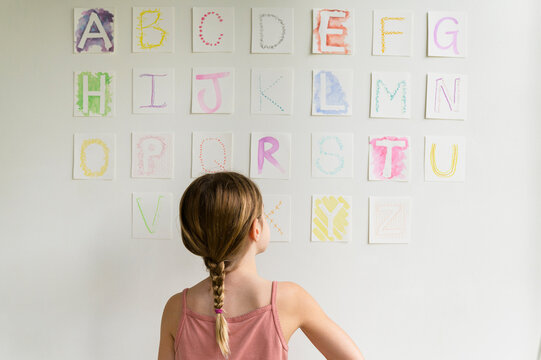 Rear view of girl (8-9) looking at alphabet on wall