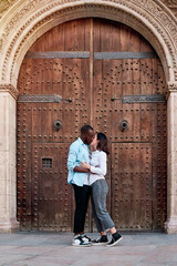 couple of young multiethnic guys kissing and laughing in front of the door of a cathedral, black guy and white girl in love