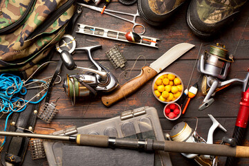 Fishing accessories. Frame with fishing boxes, reels, fishing floats, rod, compass, feeder, knife, fishing boots and fish string on wooden background. © Nikolay N. Antonov