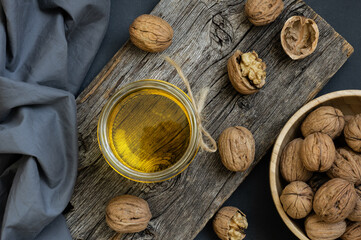 Glass jar of walnut oil with dry walnuts on rustic table
