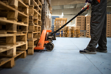 Working at warehouse. Low angle view of unrecognizable worker lifting palette with manual forklift.