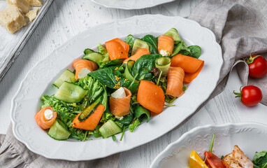 Fresh salad with salmon fish, cucumbers, feta cheese, carrots, lettuce, spinach and sauce on plate over light wooden background. Healthy food, clean eating, dieting, top view